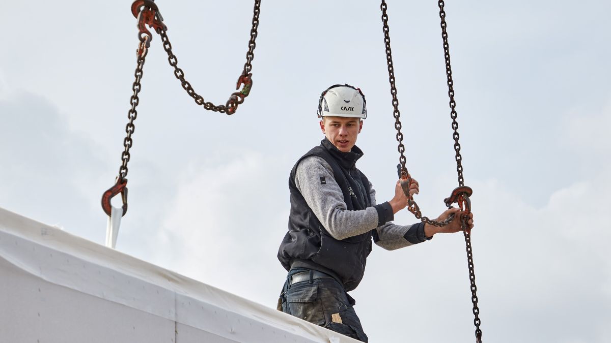 Bissantz realisiert bei Baufritz ein Planungsprojekt mit Hebelwirkung - Das Bild zeigt einen Bauarbeiter, der an einer Kette ein größeres Bauteil zu einem Fertigteil ablässt.